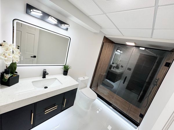Bathroom with a floating black vanity, a lit mirror and a dark glass shower