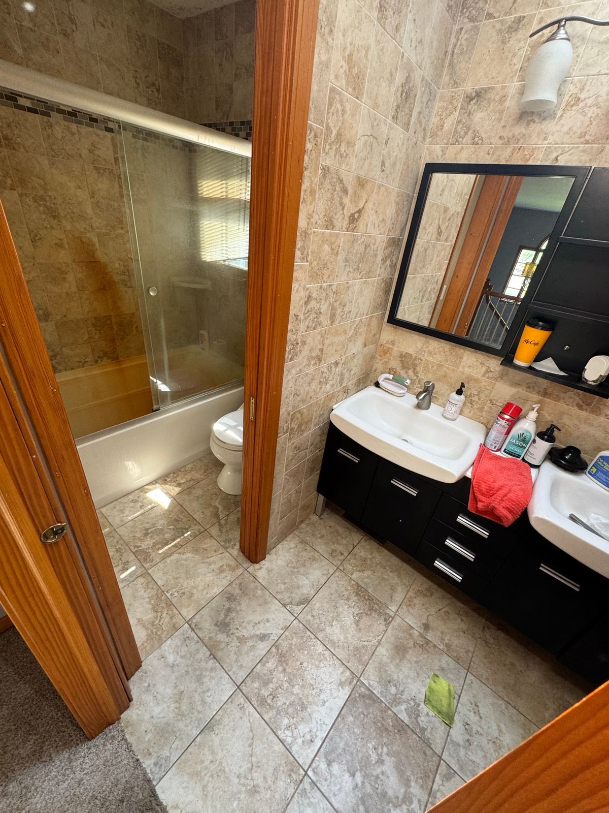 Bathroom before the remodel, with a dark vanity and travertine-look floor tile