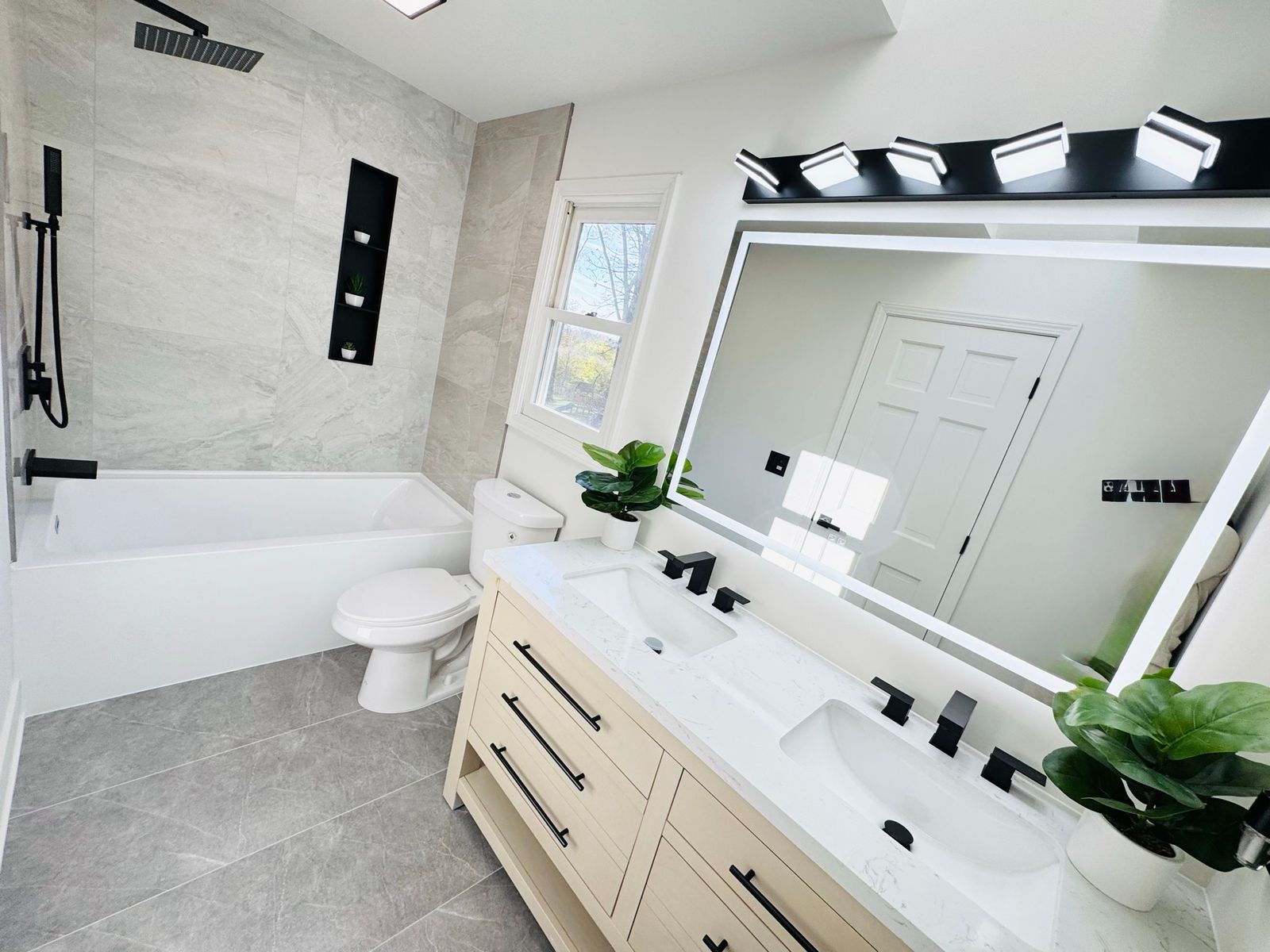 Bathroom after the remodel, with a white double vanity, a large lit mirror and gray tile