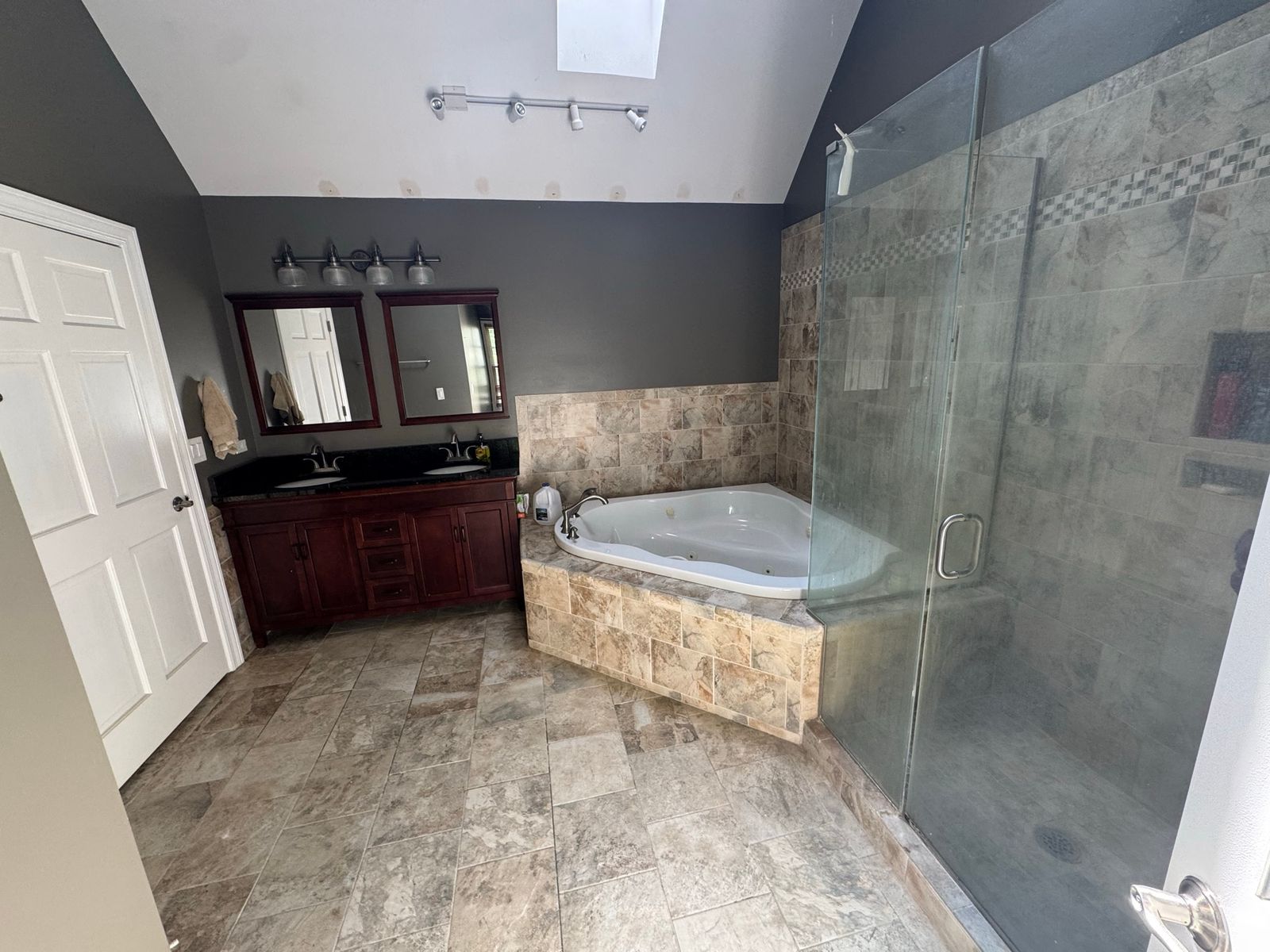 The same bathroom before, with dark vanity cabinets, a corner jetted tub and a vaulted ceiling with a skylight