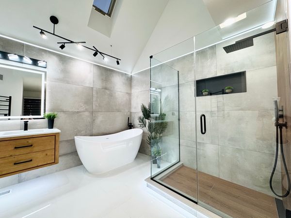 The same bathroom after, with a freestanding tub, a walk-in glass shower and a wood-tone vanity