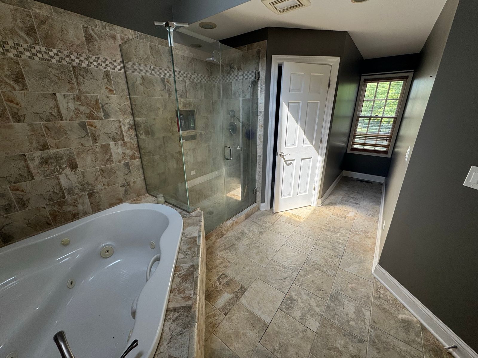 Bathroom before the remodel, with a corner jetted tub, brown tile and a glass shower