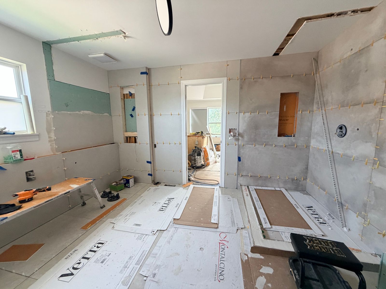Bathroom during the work, with large tile on the walls and building materials on the floor