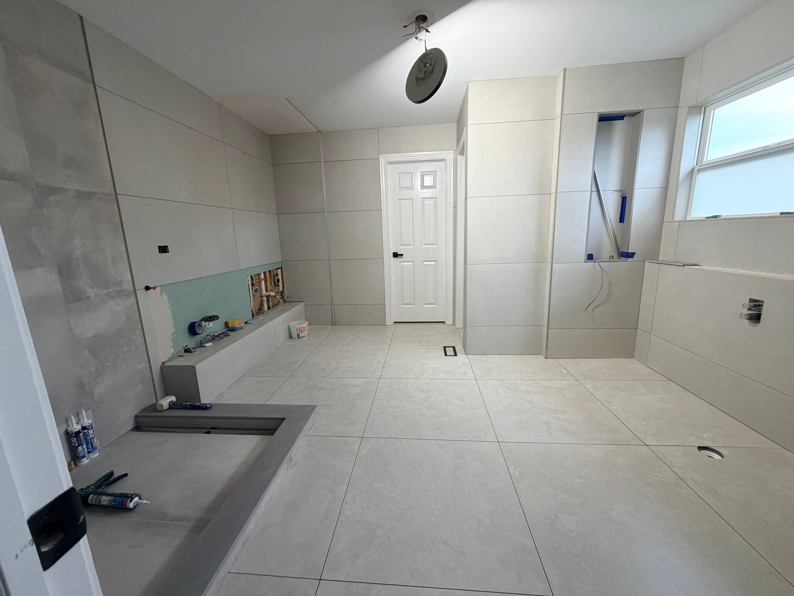 Bathroom during the work, with gray tile laid and the shower area still being built