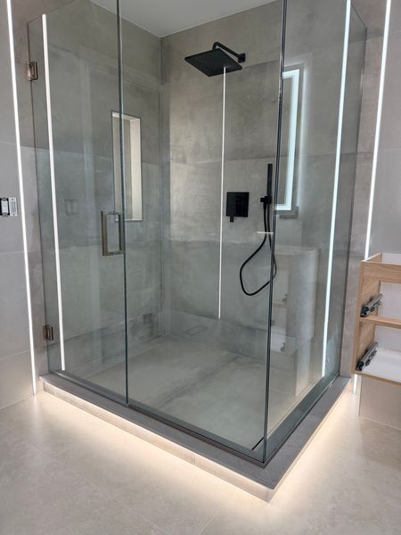 Frameless corner glass shower with a black rain head and a light strip along the base