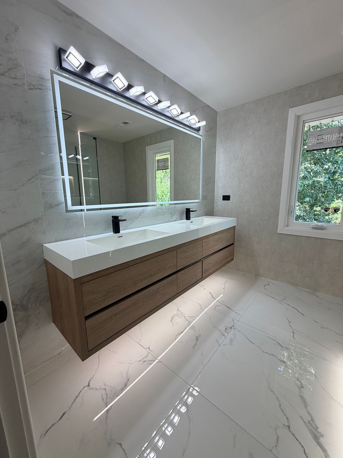 Double floating wood-tone vanity under a large lit mirror on a glossy marble-look floor