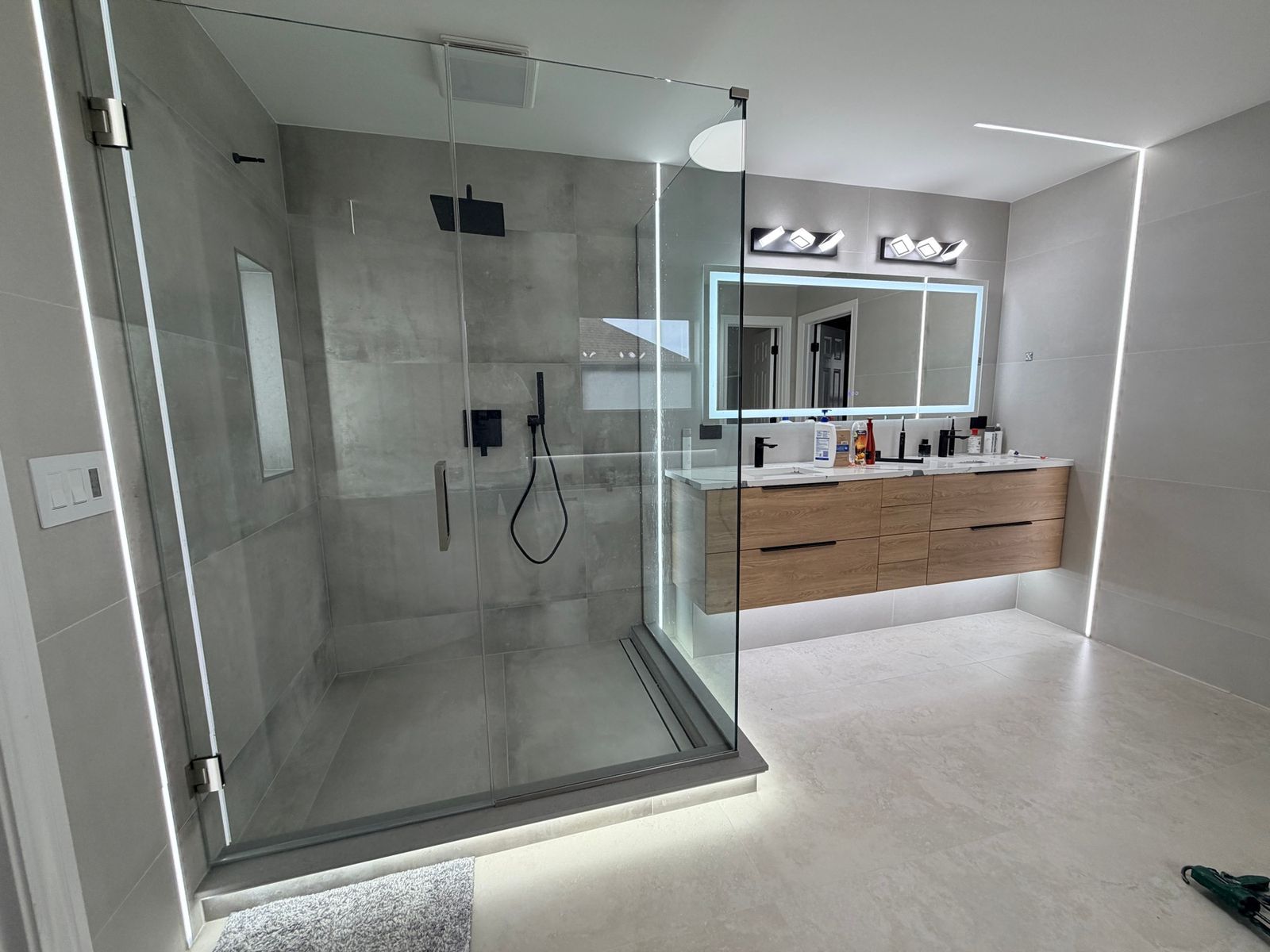 Bathroom with a corner glass shower, a floating wood-tone vanity and a lit mirror