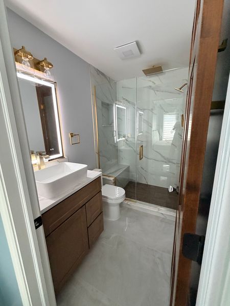 Guest bathroom with a dark wood vanity, a lit mirror and a glass shower
