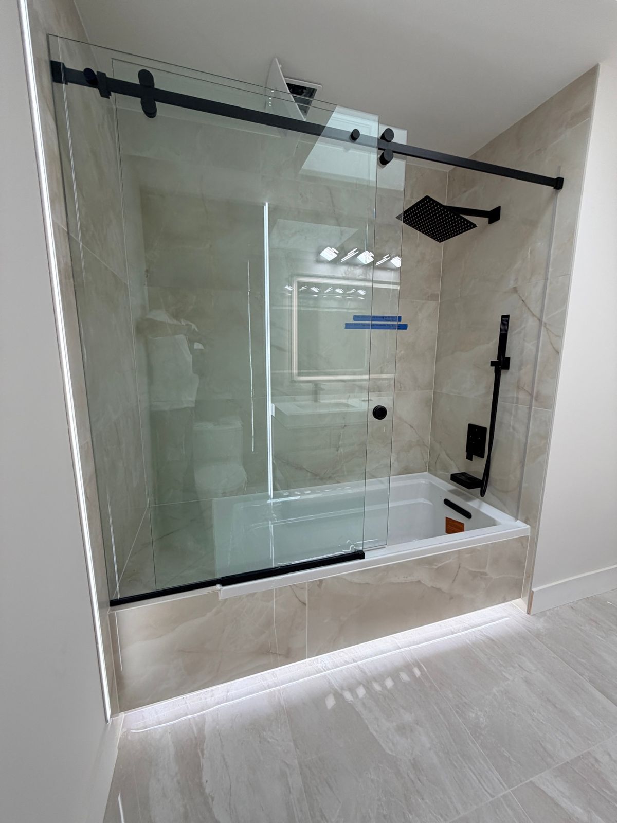 Tub-shower with black fixtures behind a sliding glass door and a light strip at its base