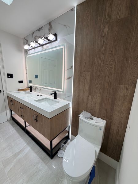 Bathroom vanity with a lit mirror beside a wood-look tile accent wall