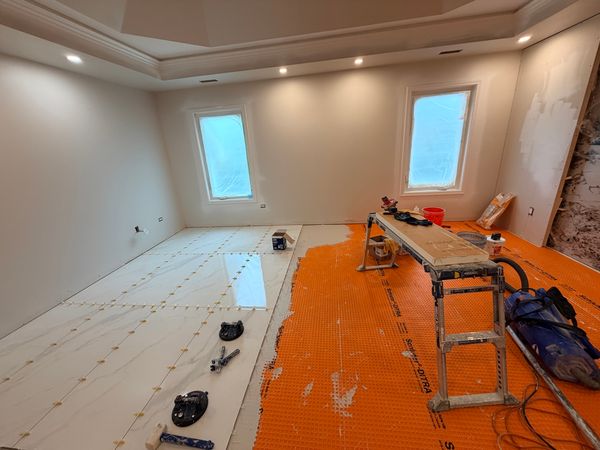 Bedroom during the work, with marble-look tile being laid beside an orange membrane and tools on a bench