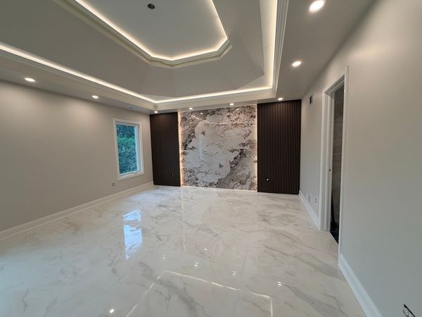 Bedroom after the work, with a marble-look floor, a lit tray ceiling and a slab-tile accent wall