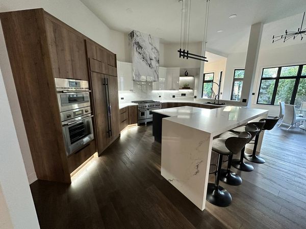 Kitchen with wood-grain tall cabinets, white gloss uppers and a white island with bar stools