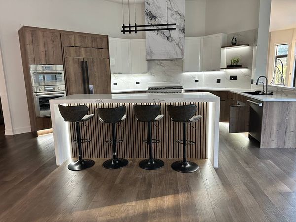 Waterfall island with a wood slat-panel base and four bar stools, with a slab-look range hood behind