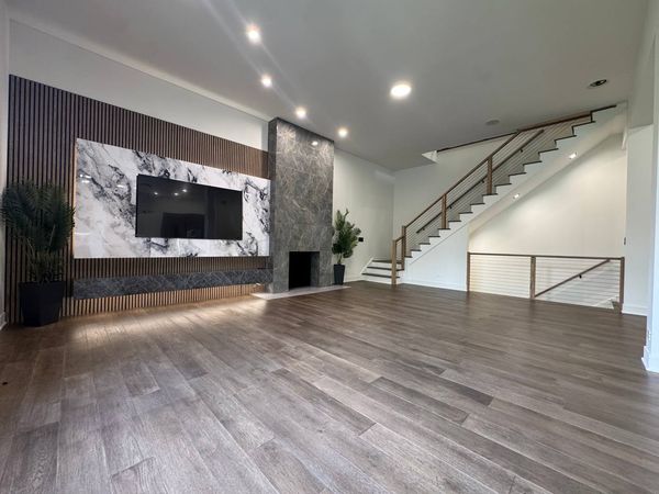 Living room with a wood slat wall, a marble-look TV panel, a stone-look fireplace surround and stairs with a cable railing