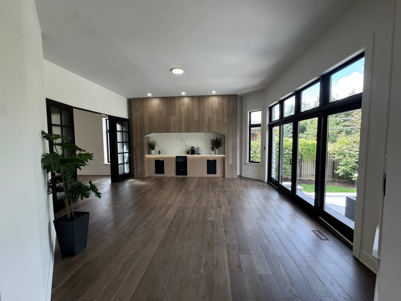 Open living area with a wood-look feature wall, a niche and large black-framed windows and doors
