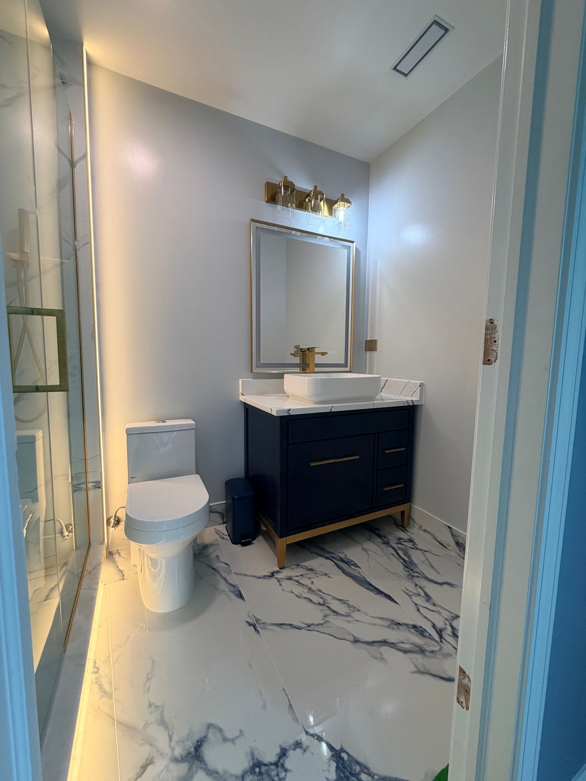 Guest bathroom with a navy vanity, brass legs and a white marble-look floor with dark veining