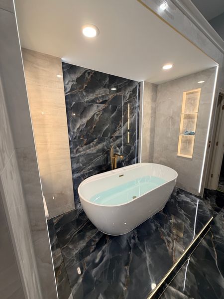 Freestanding white tub in front of a dark onyx-look tile wall and a lit niche