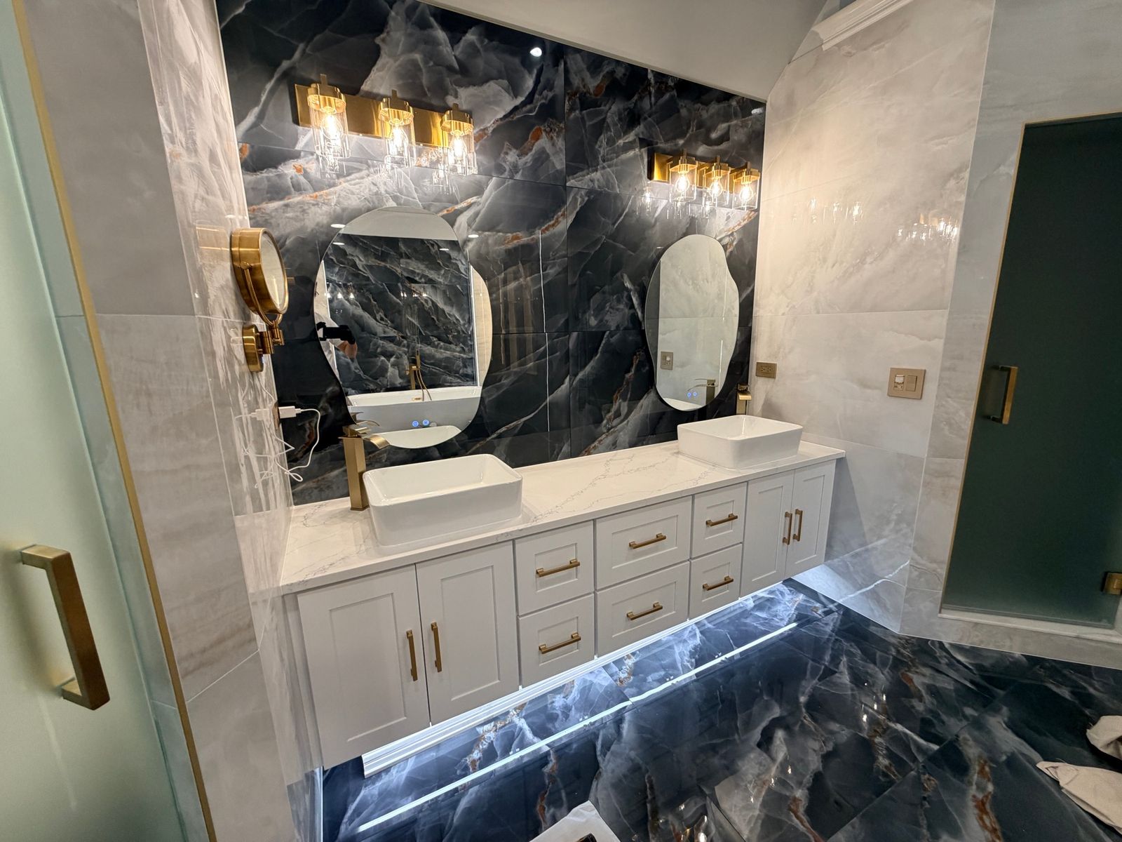 Double vanity with two vessel sinks, round mirrors and brass wall lights on a dark tile wall