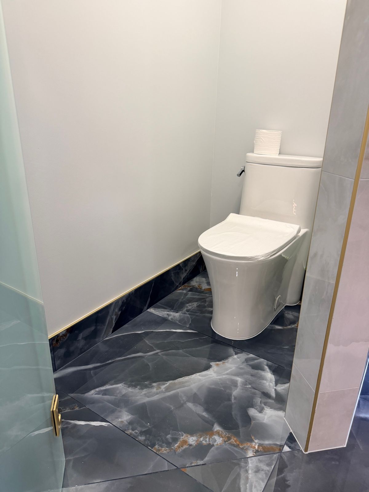 Toilet in a corner with dark onyx-look tile on the floor and lower wall