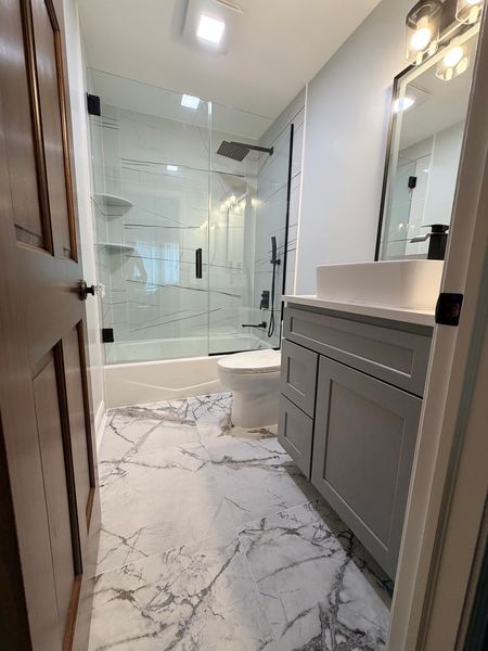 Bathroom with a gray shaker vanity, a tub-shower and a marble-look floor