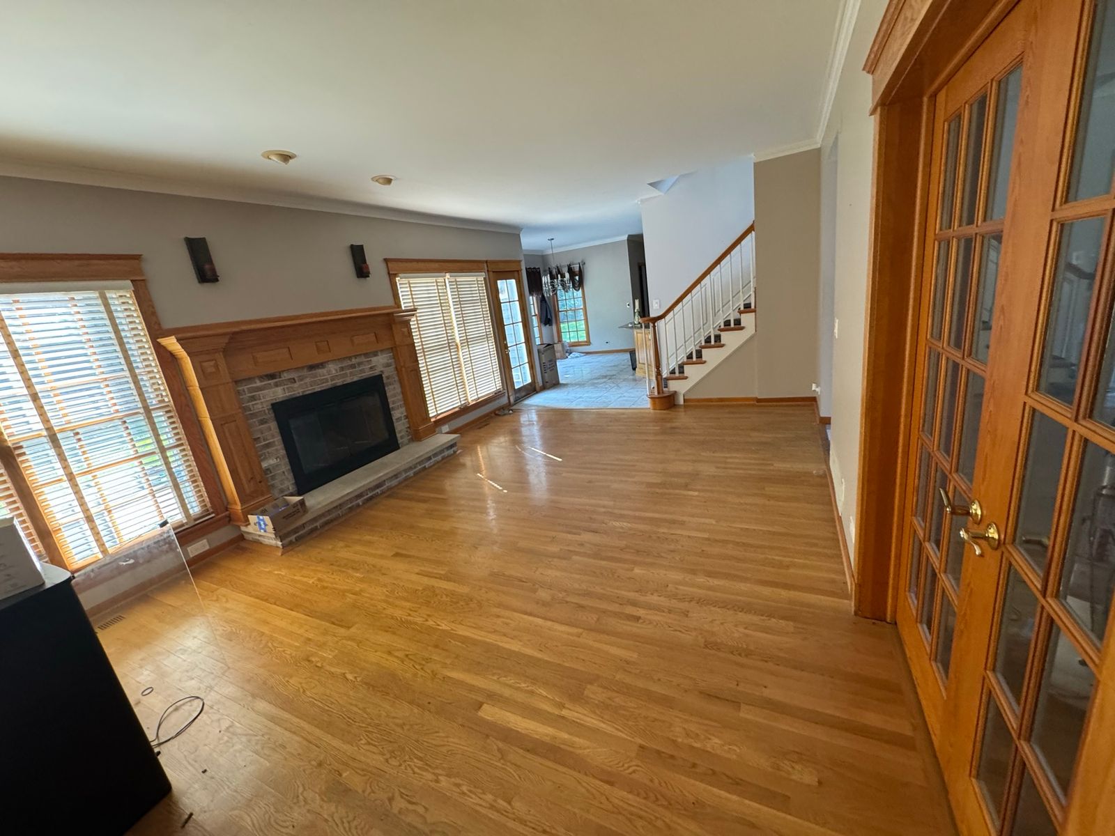 Living room before, with honey-oak floors, a fireplace with a wood mantel and French doors