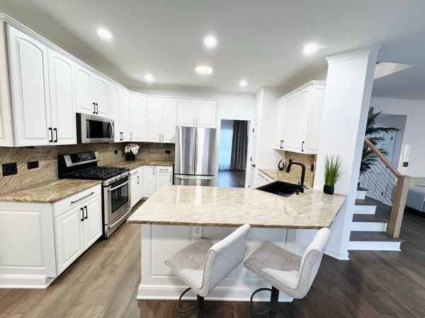 Kitchen after the remodel, with white shaker cabinets, light countertops and a plank floor